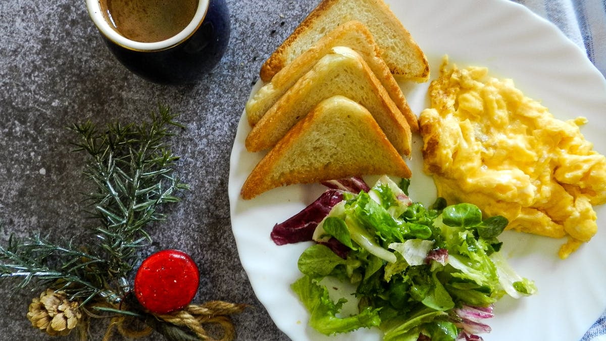 A breakfast plate with scrambled eggs, toast, salad, and coffee on a marble surface.